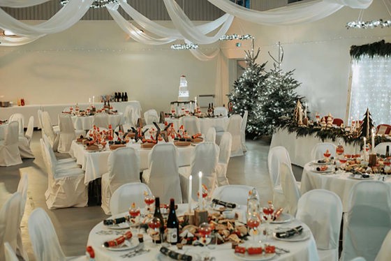 Dinner set up at wedding in white room with Christmas trees, swags of fabric on ceiling and grazing boards in the middle of each table